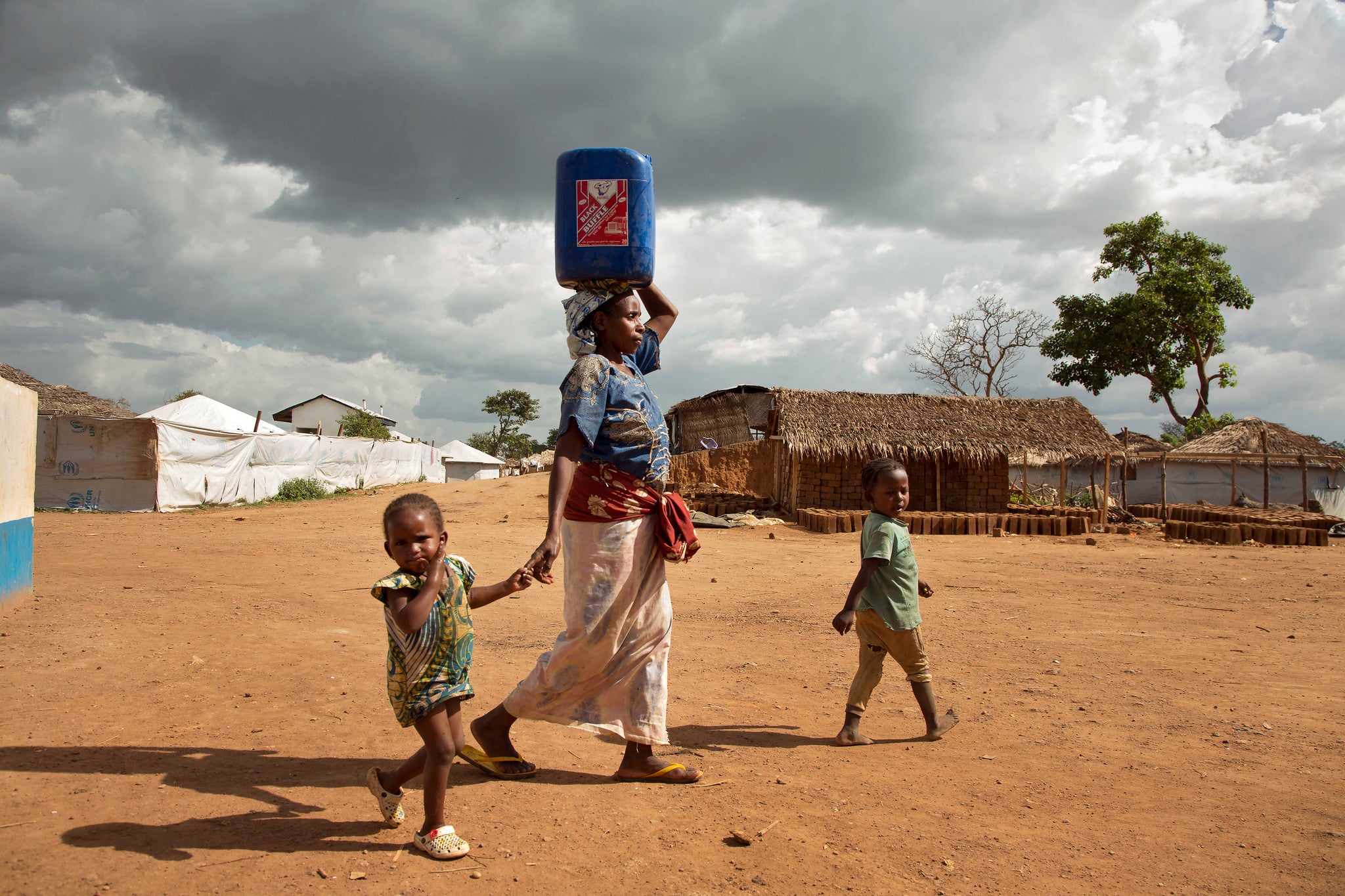 A woman carries a large jug of water through Gado refugee camp