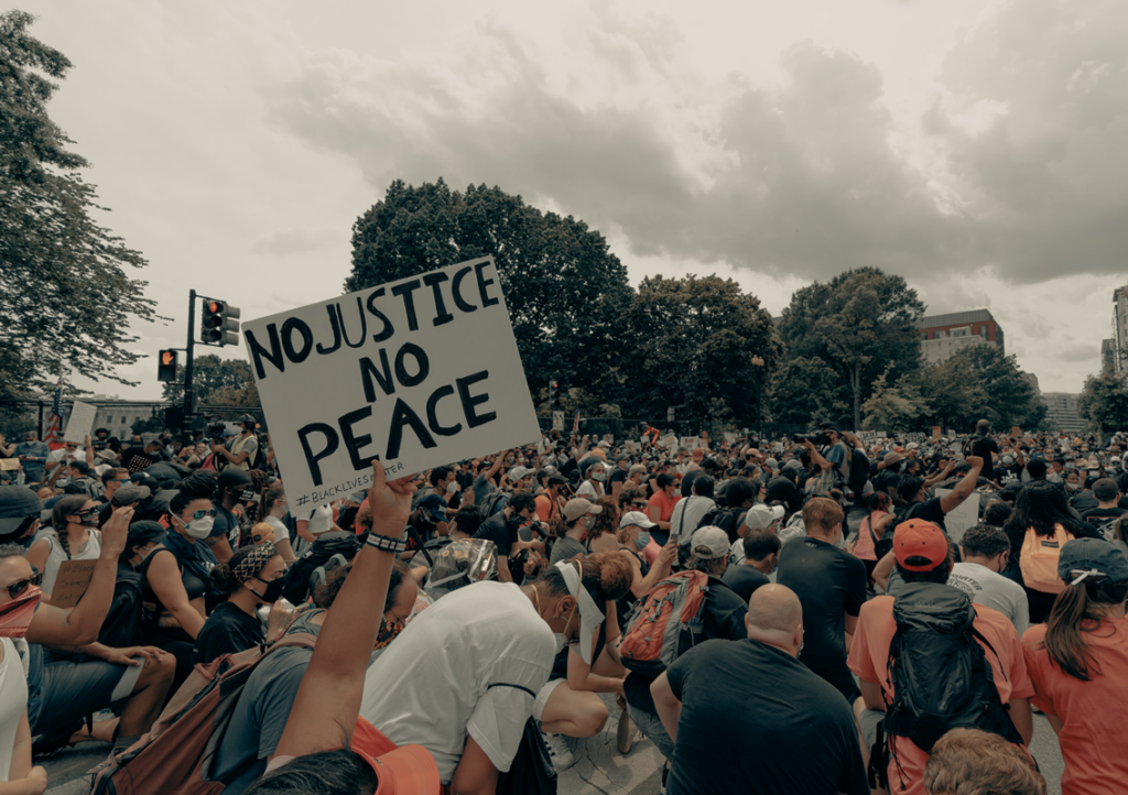 Black Lives Matter protest. Multitude of people gathered (all ages, races and genders), a sign says " No Justice, No Peace"