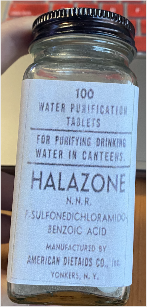 Recreation of a bottle with 100 water purification tablets. The label states that the purpose is "for purifying drinking water in canteens". The label includes the brand name, the scientific formula of the tablets, the name of the manufacturer and the place where it was produced