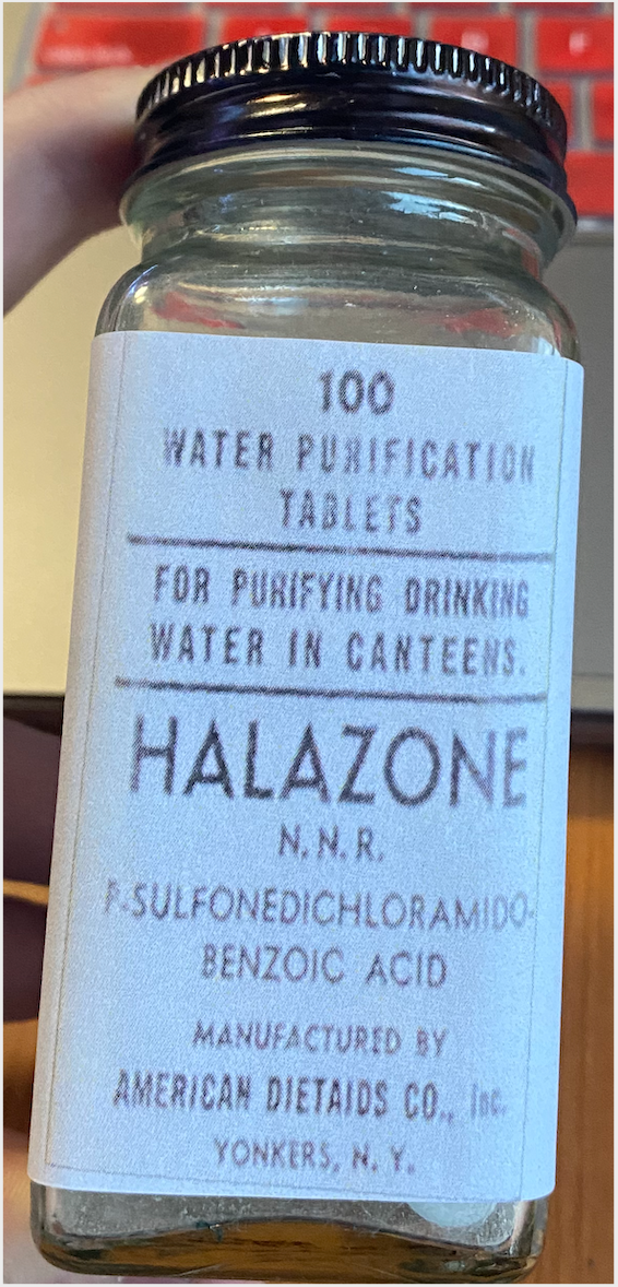 Recreation of a bottle with 100 water purification tablets. The label states that the purpose is "for purifying drinking water in canteens". The label includes the brand name, the scientific formula of the tablets, the name of the manufacturer and the place where it was produced