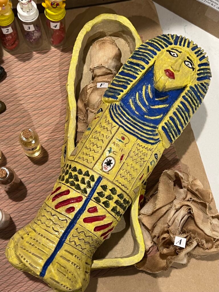 Hand-made clay sarcophagus displaying the final wrapped version of the mummy (the lid is open)