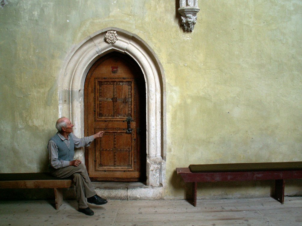 Old man sitting at the door of a fortified Church