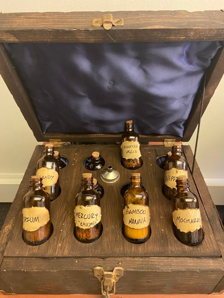 Recreation of an apothecary crate (open), showing a dozen small bottles inside. Their labels include: "bamboo manna", "mercury 'calomel'", "mocharas", "adhatoda vasica" and "opium"