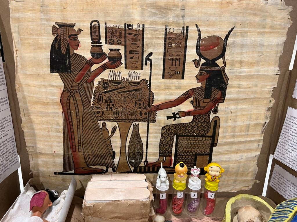 Painting showing the human or godly figures associated with death in the New Kingdom of Ancient Egypt. Underneath, there are canopic jars that were used to house their respective organs in line with the figures' spiritual significance and protective power